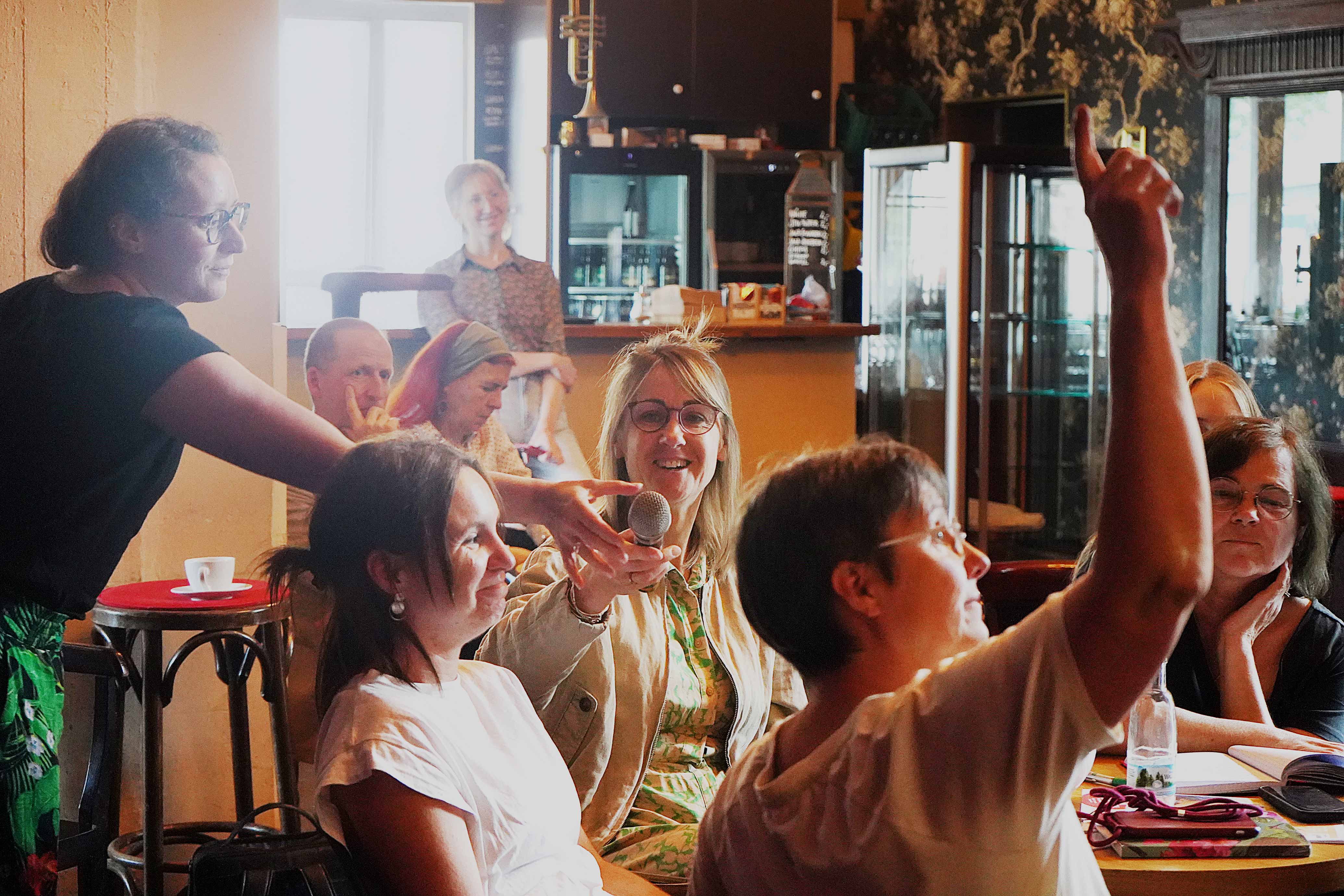 Nicole Nagorsen reicht ein Mikrofon an einen Tisch mit Frauen, wo sich Ina Paul im Vordergrund meldet