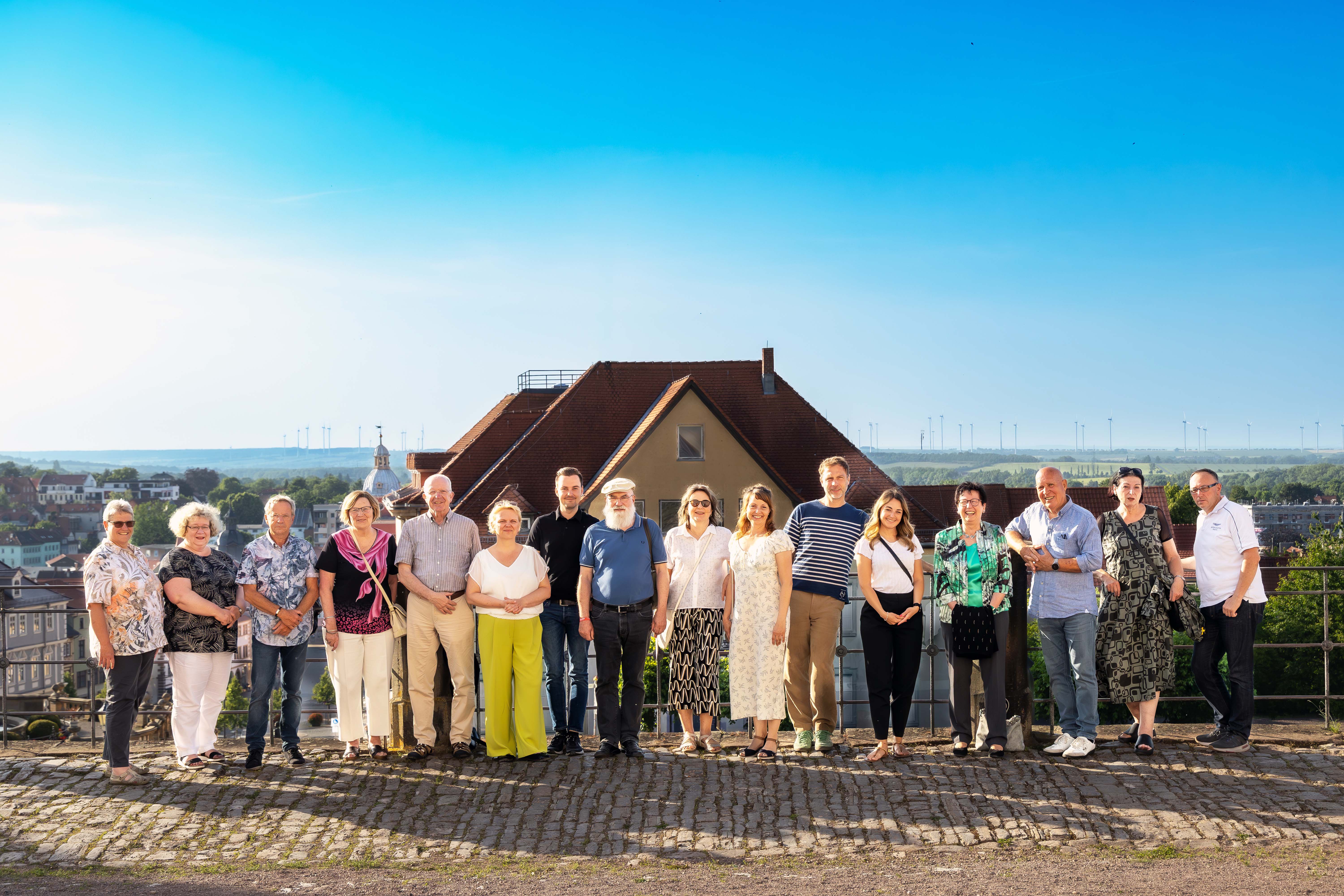 Die 16 Teilnehmenden des Kreisvorsitzendentreffen stehen nebeneinander vor der Brüstung von Schloss Friedenstein in Gotha. Hinter ihnen sieht man einige Dächer und Häuser sowie viel blauen Himmel.